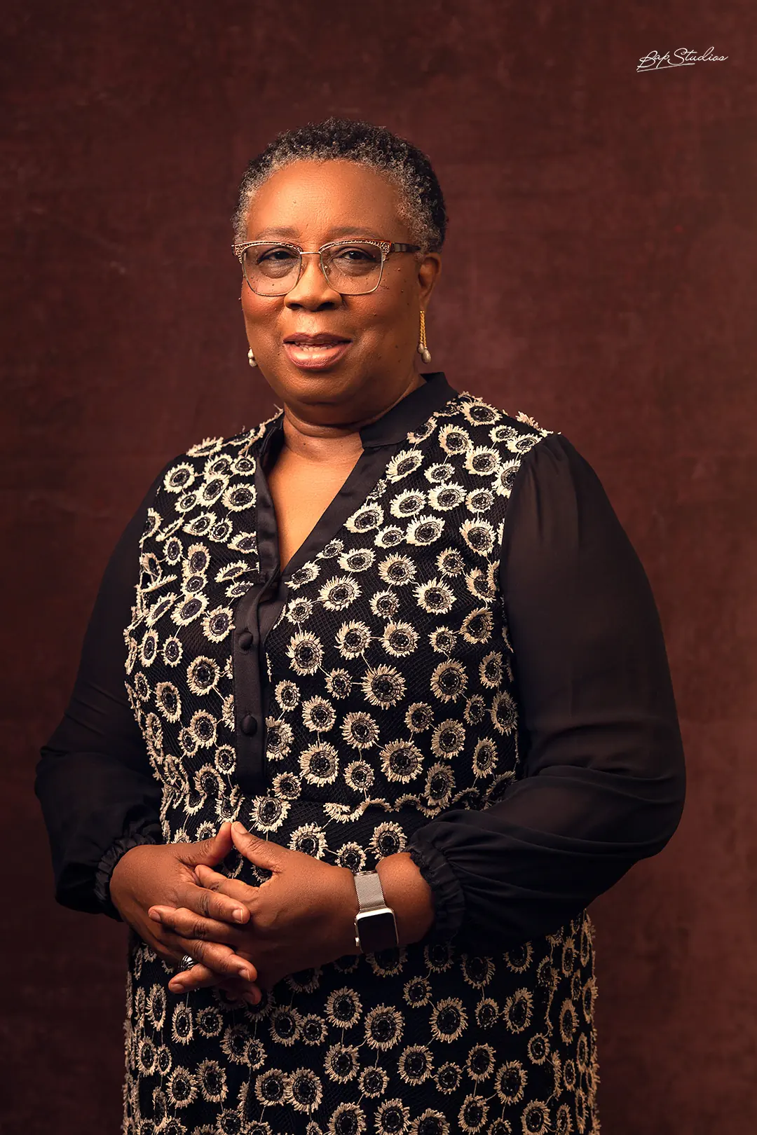 Folasade Adefisayo standing in a patterned black and gold outfit against a warm brown backdrop.